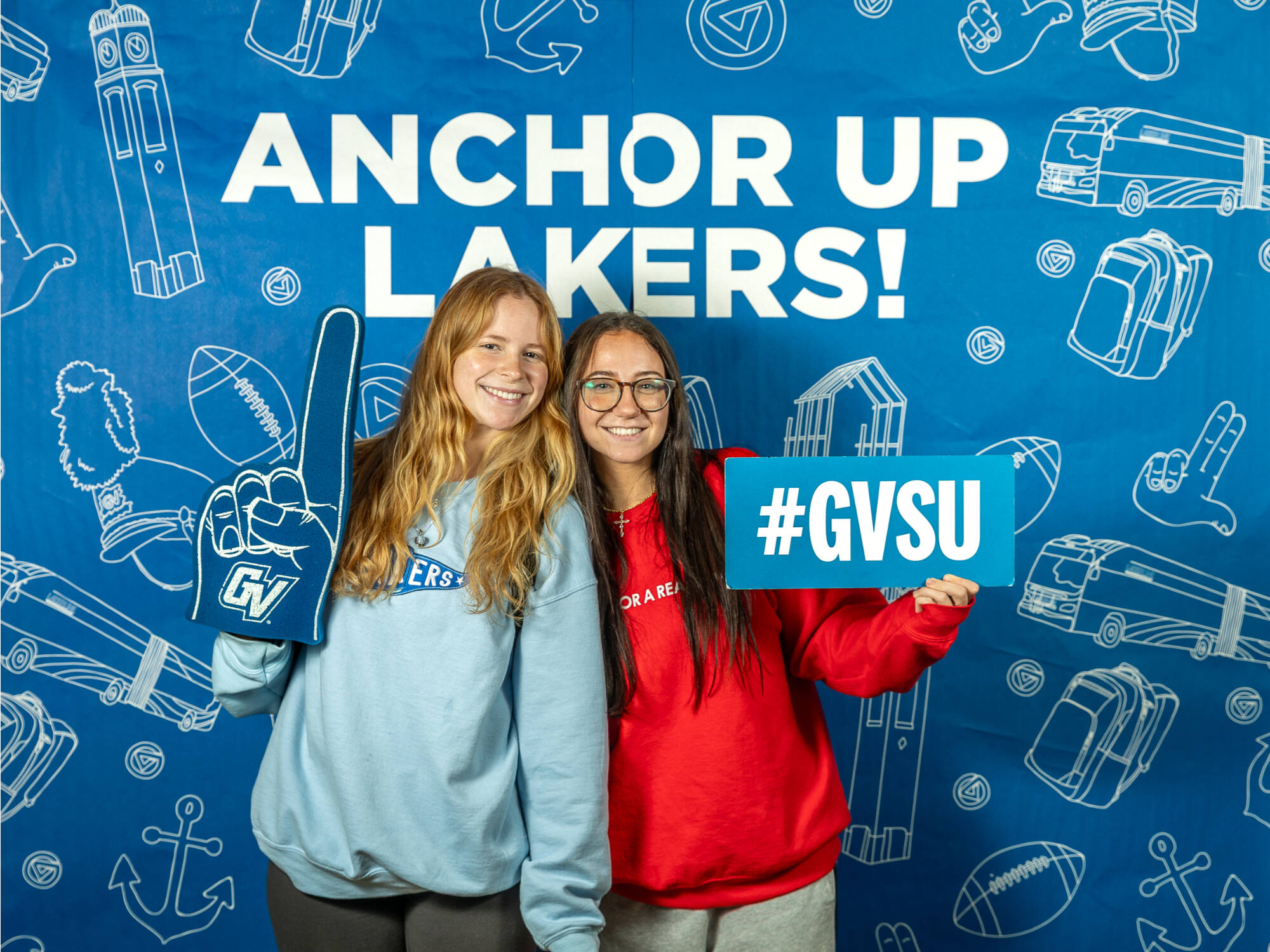 two individuals, one on the left holding a gvsu foam finger, one on the right holding a #gvsu sign